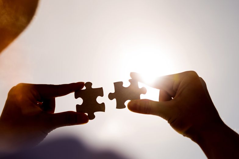 Woman hands connecting two jigsaw puzzle pieces against sunset sky.